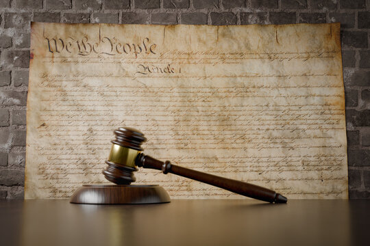 United States Constitution On Wall with Gavel Resting on Table in Front.