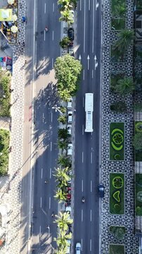 Top-down vertical drone shot of Avenida Vieira Souto in Ipanema, Rio de Janeiro, with palm trees, cars, pedestrians, and patterned sidewalk design.