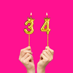 Birthday on a fuchsia background with the number 34 - Hands holding number-shaped candles
