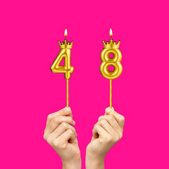 Birthday on a fuchsia background with the number 48 - Hands holding number-shaped candles