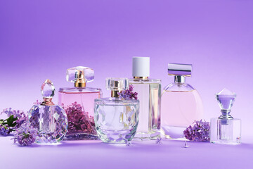 Bottles with perfumes and lilac flowers on purple gradient background, closeup