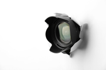 Hidden camera lens through torn hole in white paper. Space for text