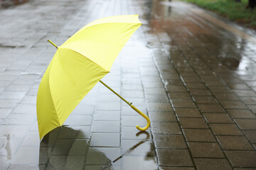 Yellow umbrella on wet asphalt outdoors, space for text
