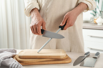 Man sharpening knife with sharpener at beige table indoors, closeup