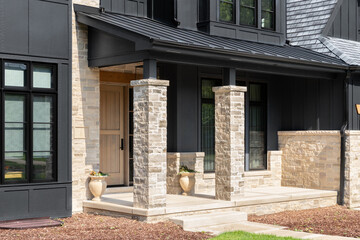 A front door detail on a home with black board and batten siding with natural stone accents and a beautiful oak front door.