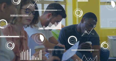 Analyzing four coworkers collaborating at office meeting table, with documents and digital charts