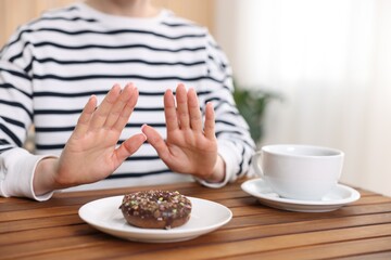 Gluten free diet. Woman refusing from donut at wooden table indoors, closeup