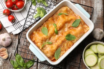 Tasty vegetarian lasagna in baking dish and ingredients on wooden table, flat lay