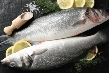 Fresh raw seabass with spices on black table, flat lay. Fish and seafood delicacies