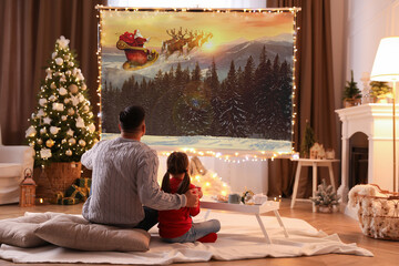 Father and daughter watching Christmas movie using video projector at home