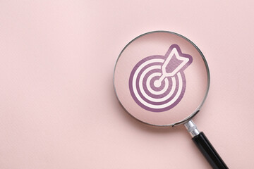Magnifying glass over target with arrow on pink background, top view