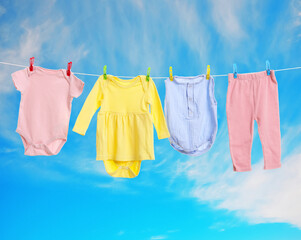 Different baby clothes drying on washing line against blue sky