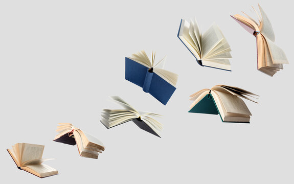 Hardcover books flying like birds against grey background