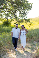 A joyful pregnant couple strolls through a sunny field, embracing nature and each other, celebrating summers beauty and the excitement of impending parenthood, while creating precious memories
