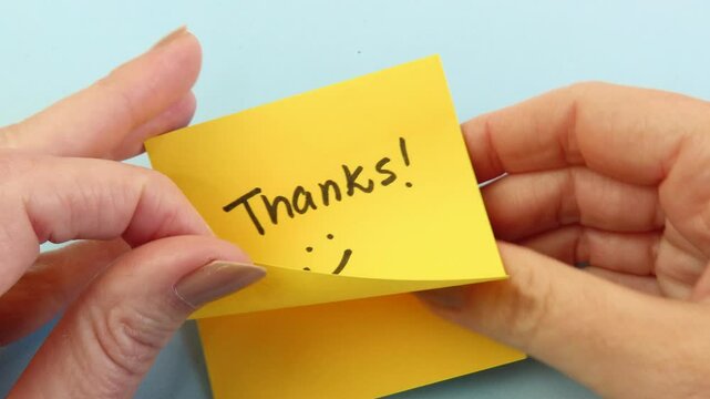 Video of woman hands preparing to stick a note with the handwritten expression "Thanks" and a smile. Hands showing a gratitude card.