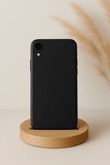 Minimalist black smartphone standing vertically on wooden round platform with neutral background and dried pampas grass, ideal for tech branding, mockup, or modern lifestyle themes

