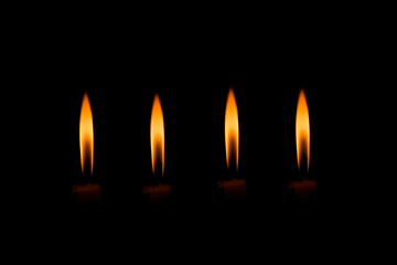 Cuatro velas encendidas alineadas sobre fondo negro en ambiente oscuro y minimalista