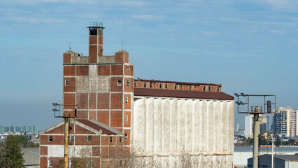 Old, abandoned brick and concrete industrial building with a large silo, standing against a blue...