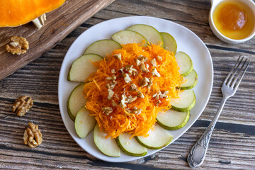 Bright healthy organic autumn harvest salad made of pears, pumpkin, walnut and honey with fork on wooden table. Top view