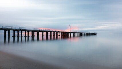 Obraz premium Sunset Reflection, Pier, Coastal Beach, Photography, Tranquil Water, Long Exposure, Serene Atmosphere