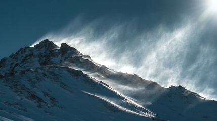 Snow-covered mountain peak with strong wind blowing snow off the ridge under a bright sun and clear blue sky.