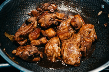 Savory chicken pork adobo simmering in a pan with rich sauce and spices.  with tender pieces marinating in a flavorful sauce. Aromatic spices fill the kitchen.