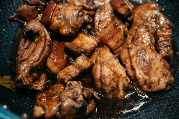 Savory chicken pork adobo simmering in a pan with rich sauce and spices.  with tender pieces marinating in a flavorful sauce. Aromatic spices fill the kitchen.