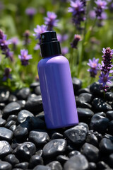 A sleek purple spray bottle rests on smooth black stones surrounded by soft focus purple flowers and green foliage