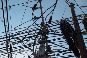 Tangled network of overhead power lines and cables against a clear blue sky.