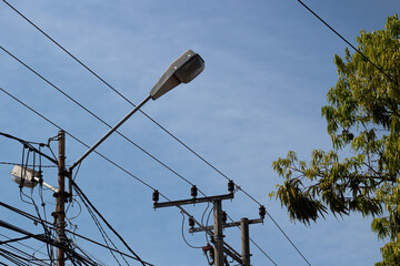 Street light, power lines, and tangled wires against a blue sky background.
