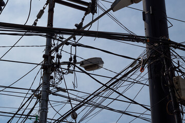 Tangled cluster of power lines and utility cables creating chaos against a blue sky.