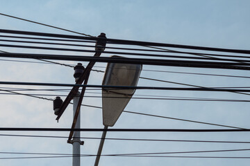 Complex network of overhead electrical wires and a street lamp against the sky.