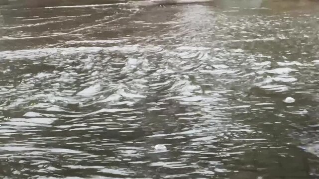 Car and motorbike rides through flooded street with splashing water, showing urban flood and rainy weather impact.