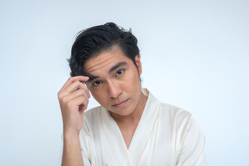 Confident young Southeast Asian man in a silk robe looks directly at the camera while adjusting his...