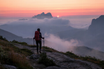 Obraz premium A dramatic landscape photograph of a solitary hiker silhouetted against a misty mountain sunrise. 
