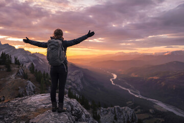 Fototapeta premium A dramatic landscape photograph of a hiker standing triumphantly on a rocky mountain summit at sunset. 
