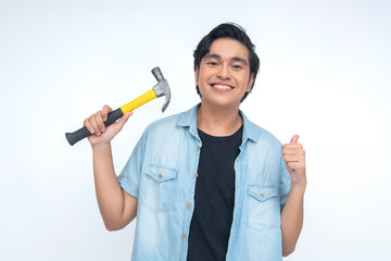 Happy Southeast Asian young man holds a hammer while smiling brightly and giving a thumbs-up...