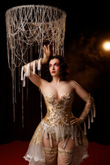 Caucasian female artist in golden Victorian-inspired corset costume, front view, dark background. Ideal for retro, Edwardian, cabaret, or theatrical performance themes.