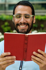 Smiling man reading a book outdoors in a park