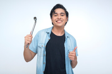 Young Filipino man in casual wear holds a tire iron and gives a thumbs up, showing confidence,...