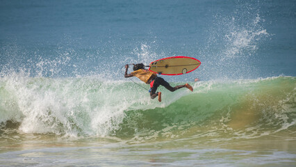 Surfer wipes out mid-air during a failed trick, with the surfboard flying alongside him above the...