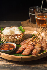Thai style grilled pork and steamed sticky rice With Jaew dipping sauce on a wooden floor