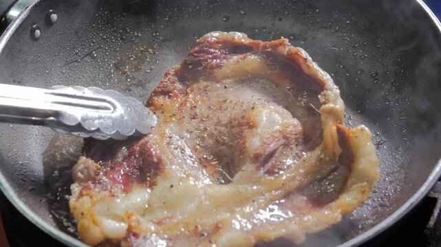  A close-up shot of a juicy ribeye steak sizzling in a hot pan, being flipped with tongs to cook evenly. The steam rises as the meat browns, showcasing the delicious cooking process.
