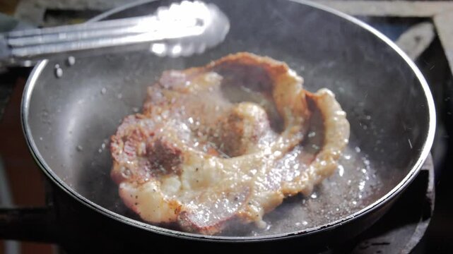  A close-up shot of a juicy ribeye steak sizzling in a hot pan, being flipped with tongs to cook evenly. The steam rises as the meat browns, showcasing the delicious cooking process.