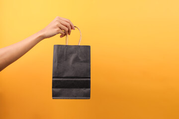 Female Hand Holding Black Paper Shopping Bag Isolated On Yellow Background