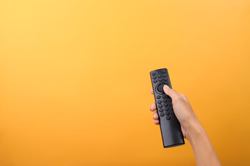 Hand Holding Black Remote Control Against Yellow Background