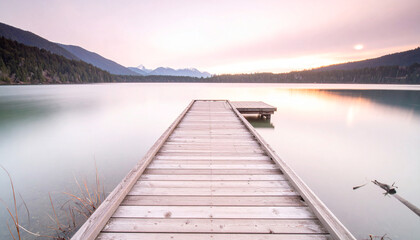 Fototapeta premium A wooden dock sits on a lake, with a beautiful view of the mountains in the background. The water is calm and clear, reflecting the surrounding trees and mountains.