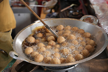 Meatballs are being deep-fried in hot oil, turning golden brown and crispy inside a large wok on a...