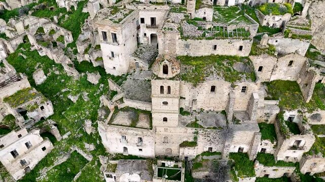 Aerial view of an abandoned medieval village of Craco, Italy on a hilltop surrounded by lush green landscape under a cloudy sky.
