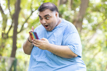 Amazed overweight indian man using smart phone. Plus size guy holding mobile phone get surprised....